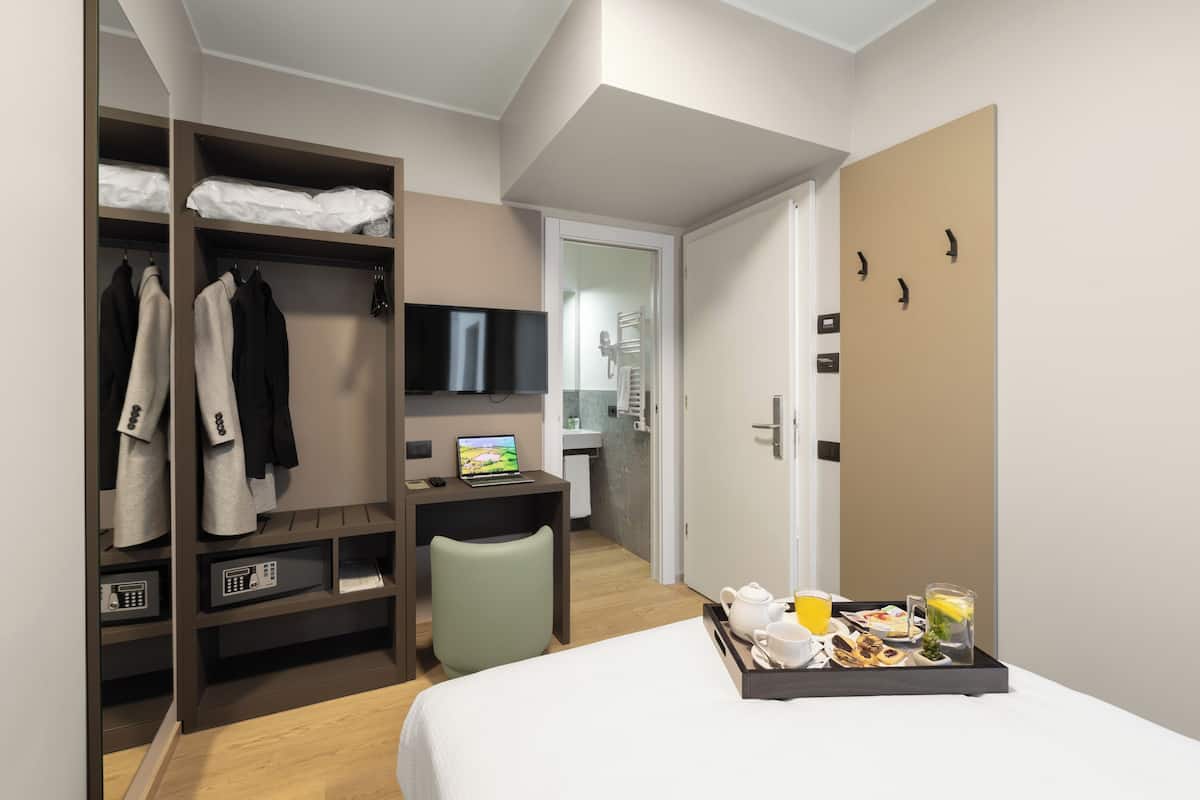 Ein Hotelzimmer mit Bett, Schreibtisch mit Laptop, Fernseher, Kleiderschrank und Frühstückswagen.