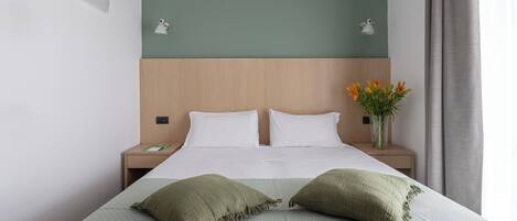 A neatly made bed with two pillows, a wooden headboard, and a green wall.