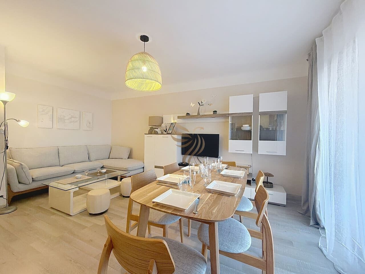 Ett modernt vardagsrum med en soffa, ett soffbord, ett matbord med plats för fyra personer och en tv som är monterad ovanför eldstaden.