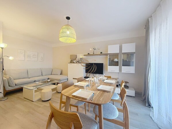 Un salon moderne comprenant un canapé, une table basse, une table à manger pour quatre personnes et un téléviseur fixé au-dessus de la cheminée.