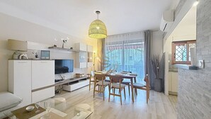 A modern living room with a dining area, a kitchen, and a large window providing natural light. - Apt3BR,AC,WiFi, sea view, parking, 3min to beach (Fréjus)