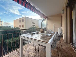 A balcony with a table set for dining, a chair, and a view of buildings in the background.