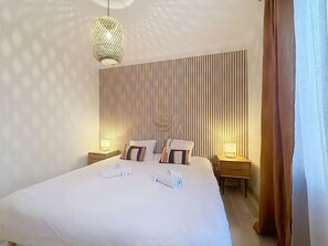 Une chambre d’hôtel avec un grand lit, deux tables de chevet, un luminaire suspendu et un mur à rayures.