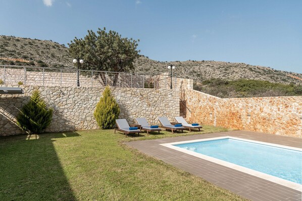 Un espace piscine agrémenté de murs en pierre, d’une pelouse verdoyante et de chaises longues.