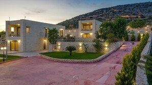 A modern two-story building with a stone facade, a well-maintained lawn, and a paved driveway. - Stone villa with private pool close to Marathi beach (Kounoupidiana, Marathi, Chania)