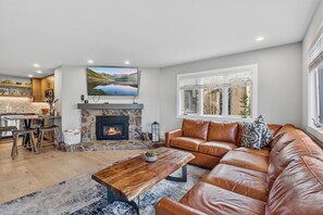 A modern living room with a stone fireplace, leather sofa, and a large TV mounted on the wall.