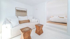 Quarto minimalista com cama branca, sofá e duas mesas de cabeceira de madeira.