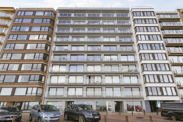 Un edificio residencial de varios pisos, con balcones, un estacionamiento y cielo despejado.