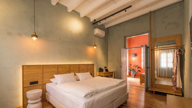 A bedroom with a wooden headboard, a large bed, bedside tables, a wooden floor, and an open door leading to another room. - It's ideal for families
or groups of up to seven people. (Chania)