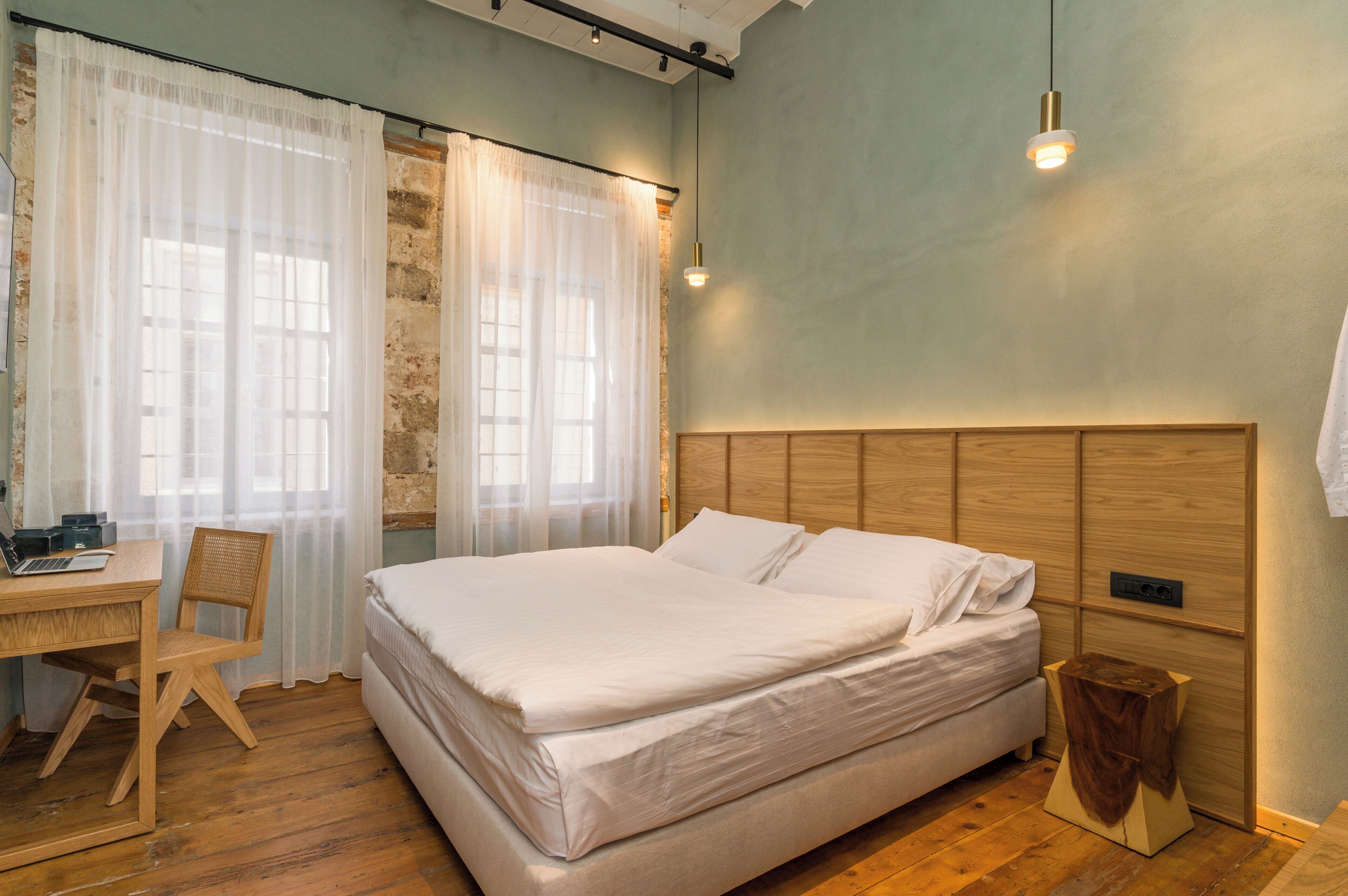 A bedroom with a wooden bed, a desk with a chair, and a small wooden stool.