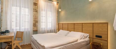 A bedroom with a wooden bed, a desk with a chair, and a small wooden stool.