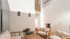 A sunlit outdoor seating area with a wooden table, two sofas, and a small potted plant. - It's ideal for families
or groups of up to seven people. (Chania)