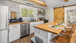 A modern kitchen with a wooden island, stainless steel appliances, and a large window with blinds. - The Creekside Pump House (Spearfish)