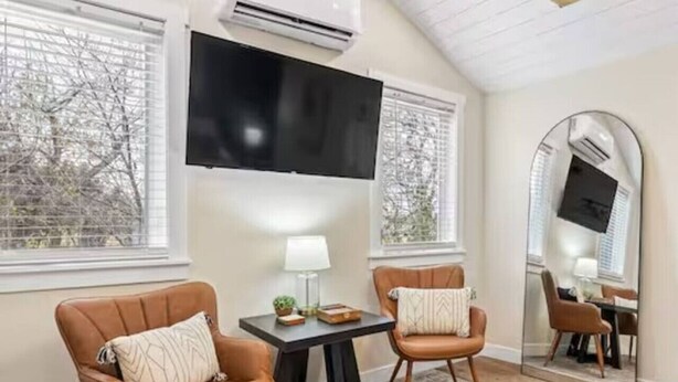 A room with two leather armchairs, a small table with a lamp, a flat-screen TV mounted on the wall, and a large mirror. - The Creekside Pump House (Spearfish)