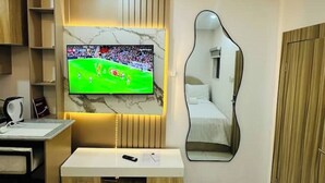 A modern hotel room with a large flat-screen TV mounted on a marble wall, a bedside table with a remote control, and a unique mirror design. - Studio(S9)@LEKKI PHASE 1, 24/7 Pwr by NgoZiLiving

 (Lekki)
