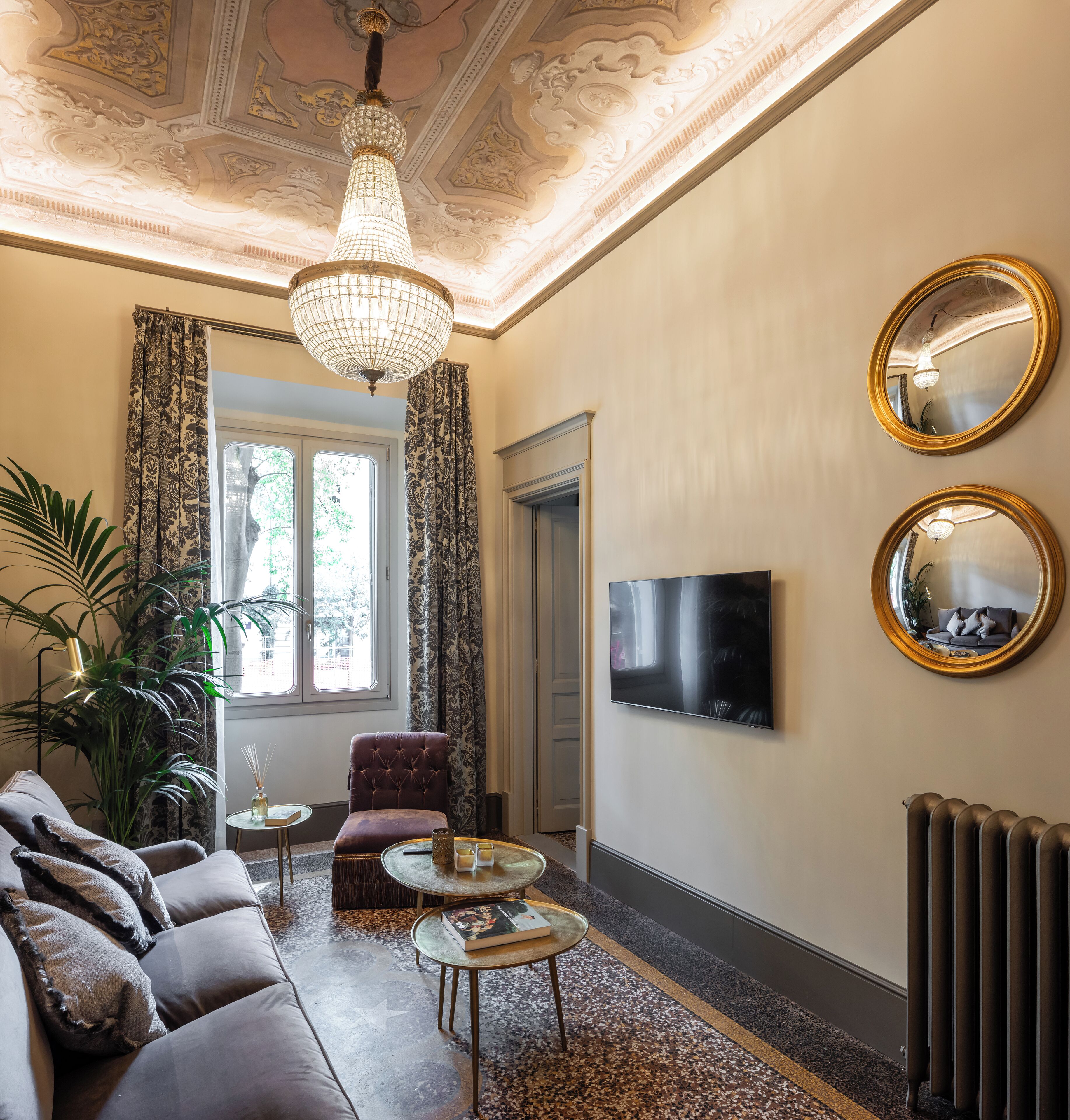 A living room with a sofa, a coffee table, a chandelier, a TV, and two mirrors on the wall.