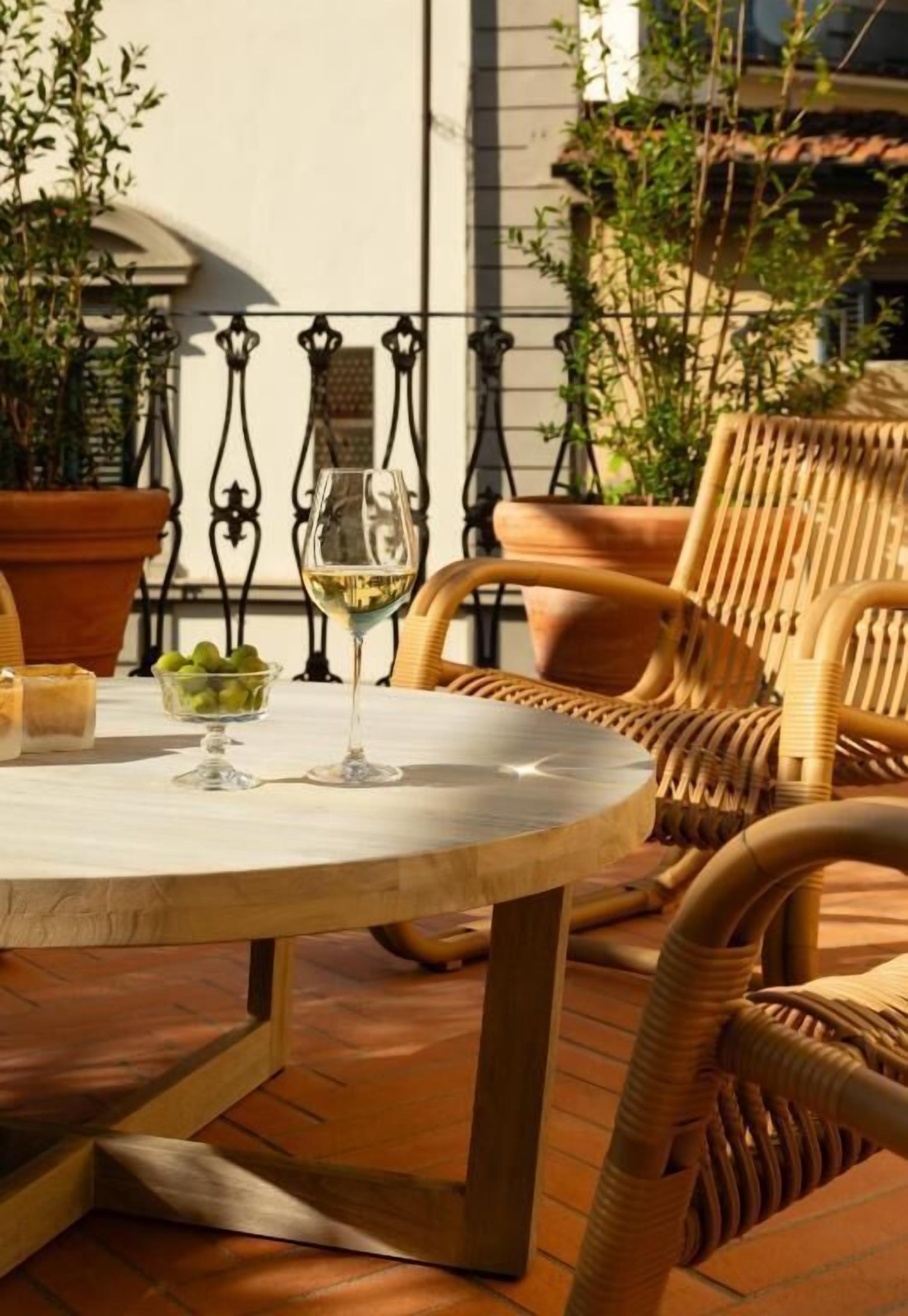 Une table ronde, un verre de vin blanc et un bol de raisins verts, le tout entouré de chaises en osier.