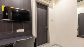 Une pièce avec un bureau en bois foncé, un téléviseur à écran plat fixé au mur au-dessus, une porte avec une poignée et une prise électrique sur le mur.