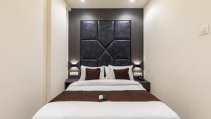 Une chambre d’hôtel moderne avec un grand lit, une tête de lit sombre, des lampes de chevet et une télécommande posée sur le lit.