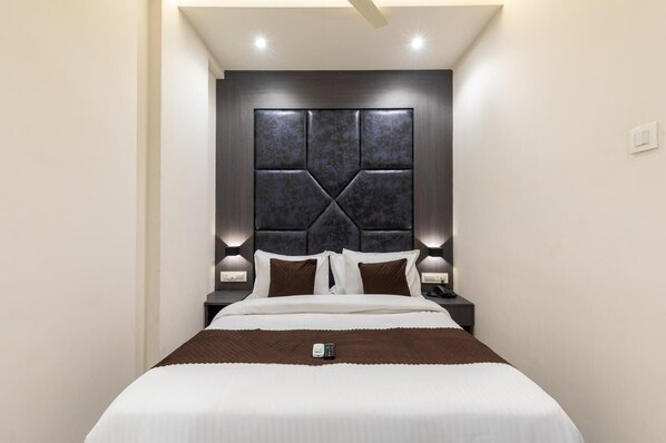 A modern hotel room with a large bed, a dark headboard, bedside lamps, and a remote control on the bed. - Hotel Artilla Borivali (Mumbai)
