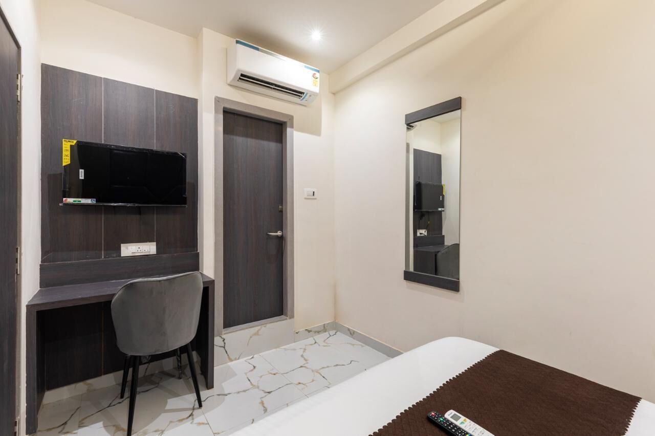 Habitació d'hotel amb escriptori de fusta fosca, una cadira, un llit amb manta marró, televisió plana penjada a la paret i un mirall gran.