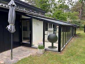 Une maison moderne dotée d’un patio entièrement vitré, d’une façade noire et d’un jardin agrémenté d’un objet sphérique.