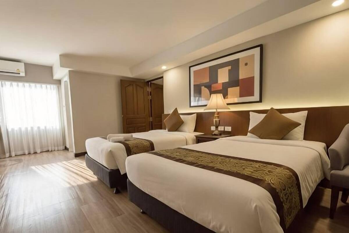 Une chambre d’hôtel avec deux lits, une armoire en bois, un tableau au mur et une lampe sur la table de chevet.