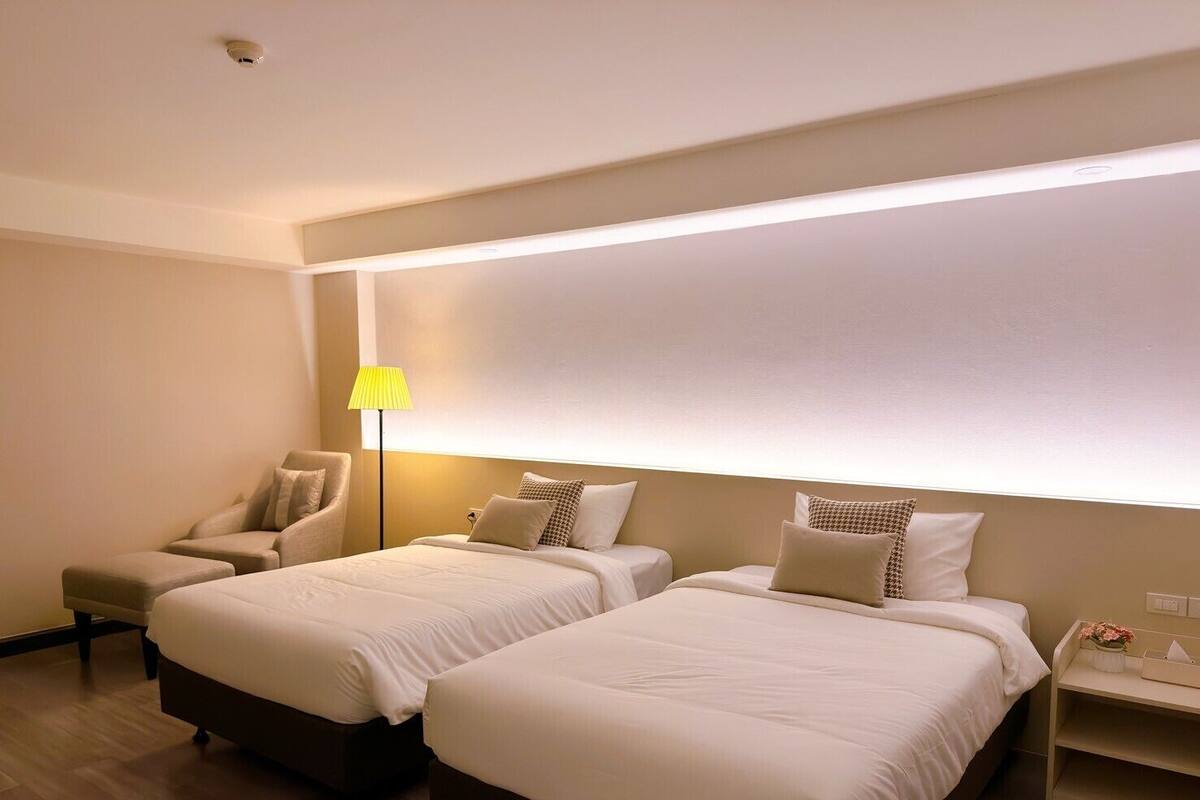 Une chambre d’hôtel avec deux lits, une chaise, une table de chevet et une lampe.