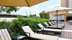 An outdoor lounge area with striped lounge chairs and tables, surrounded by greenery and umbrellas.