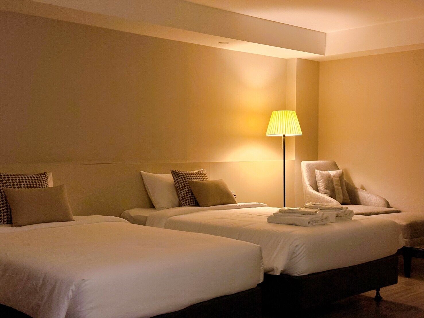 A hotel room with two beds, a chair, and a lamp.