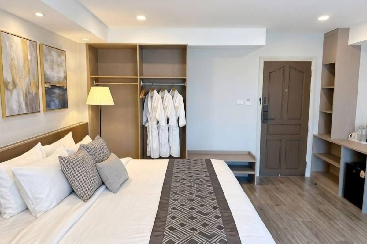 Habitación de hotel con cama, vestidor, escritorio y puerta que da a otra habitación.