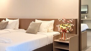 A hotel room with two beds, a nightstand, a vase of flowers, and a mirror.