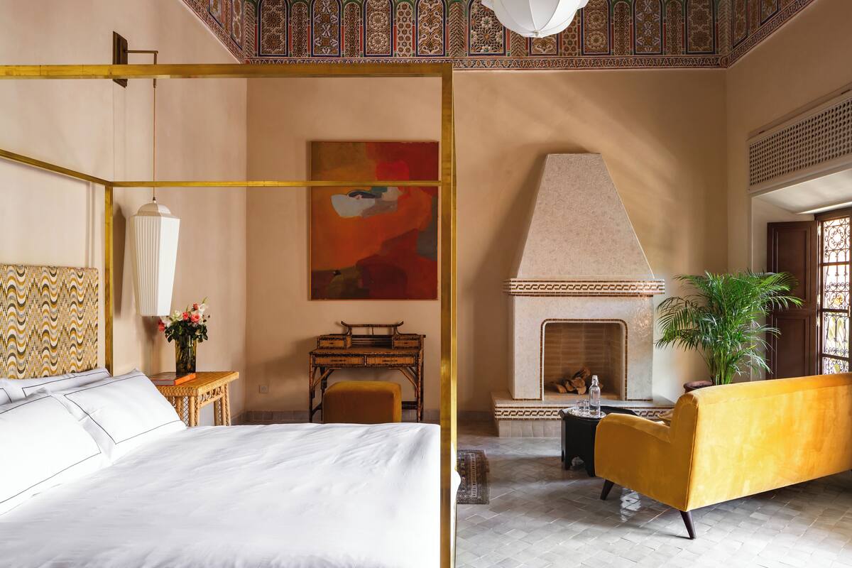 A room with a four-poster bed, a sofa, a fireplace, and a ceiling with intricate patterns.