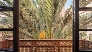 A balcony with a view of palm trees, a patterned fence, and wicker furniture. - This Time Tomorrow in Marrakech (Marrakech)