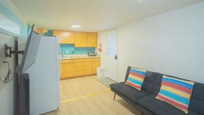 A compact living space with a kitchenette, a sofa with striped cushions, and a small trash bin.