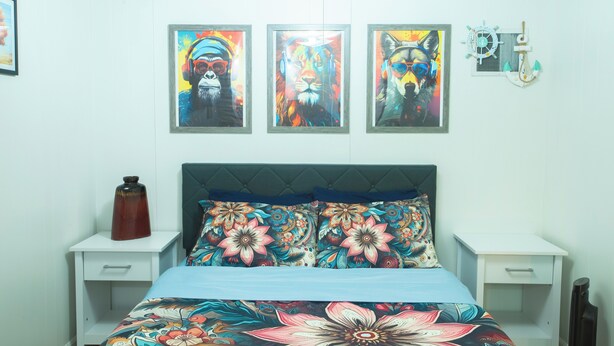 A bedroom with a bed, two nightstands, and three framed artworks on the wall.