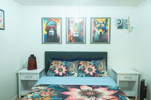 Une chambre à coucher avec un lit, deux tables de chevet et trois œuvres d’art encadrées accrochées au mur.