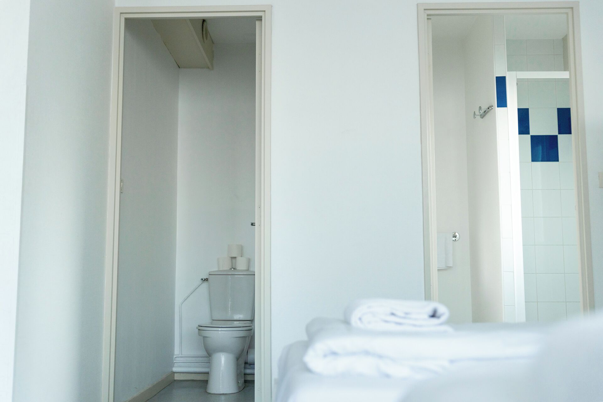 Baño con inodoro, zona de ducha y cama con una toalla doblada con cuidado.