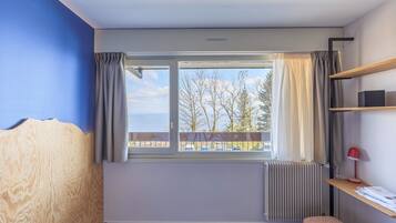 A room with a large window, a radiator, a bench, and a shelf with a lamp.