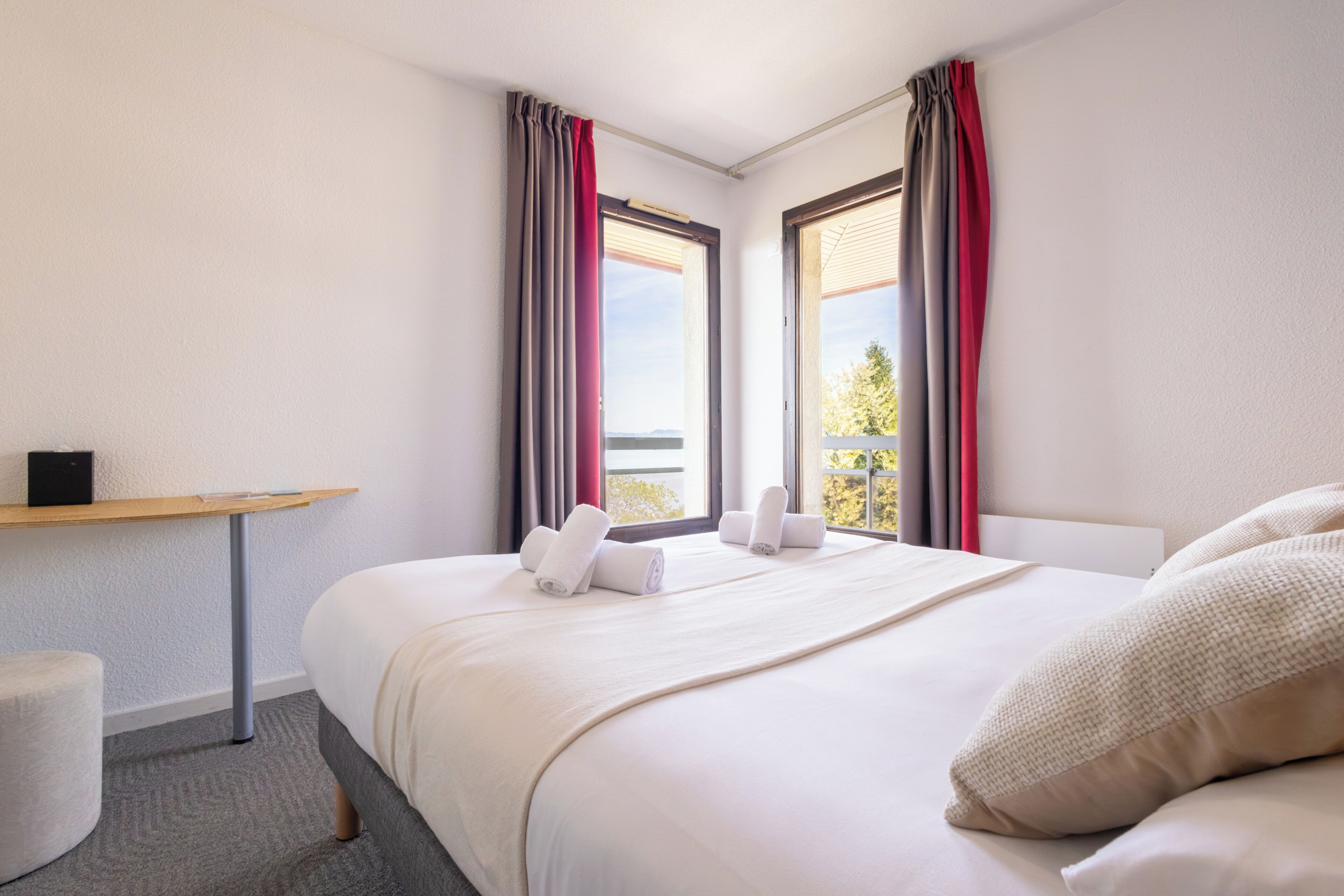 Een hotelkamer met een bed, twee ramen voorzien van gordijnen, een kleine tafel en een stoel.