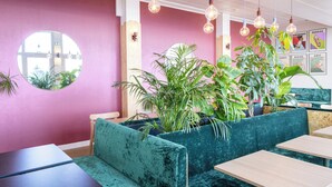 Un restaurant avec des sièges rembourrés de couleur turquoise, des lampes suspendues et un mur rose orné de photos de sport encadrées.