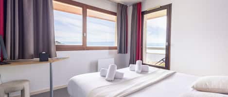 Una habitación de hotel con cama, escritorio, silla y ventana con cortinas.