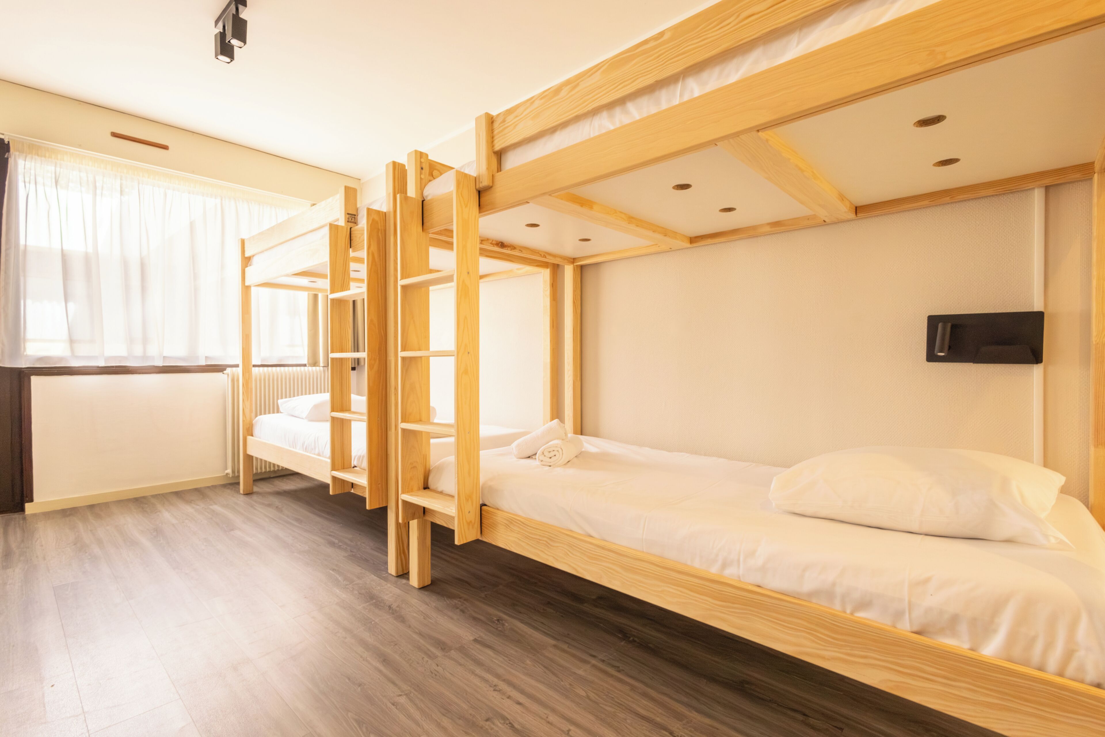 Dormitorio con literas, una escalera de madera, un escritorio y un televisor instalado en la pared.