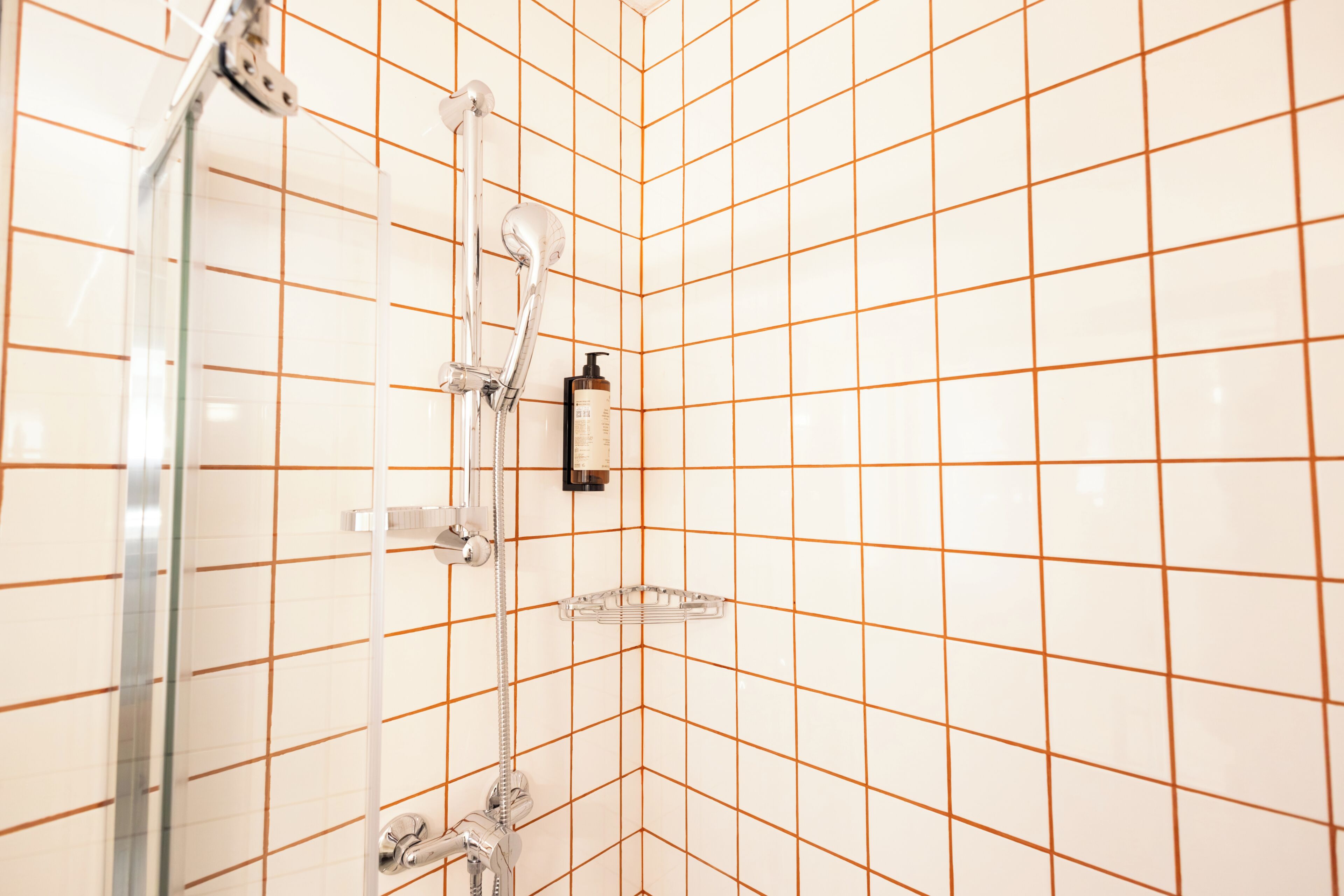 A bathroom with a shower, tiled walls, and a soap dispenser.