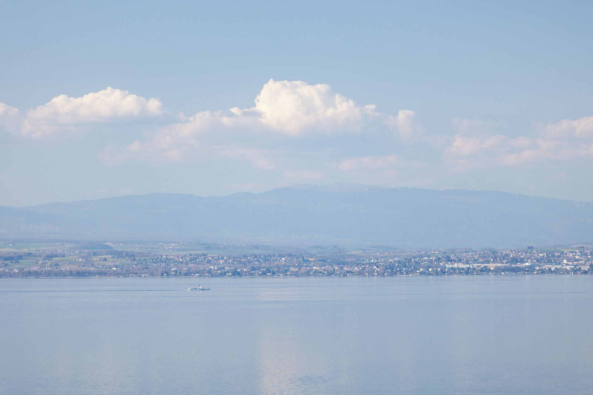 A coastal cityscape with a calm sea, distant mountains, and a small boat.
