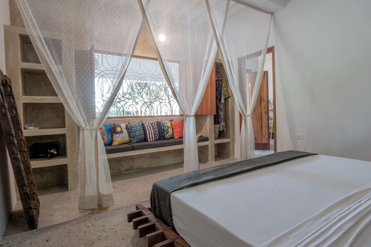 A bedroom with a bed, a window with a view, a shelf with pillows, and a wardrobe.