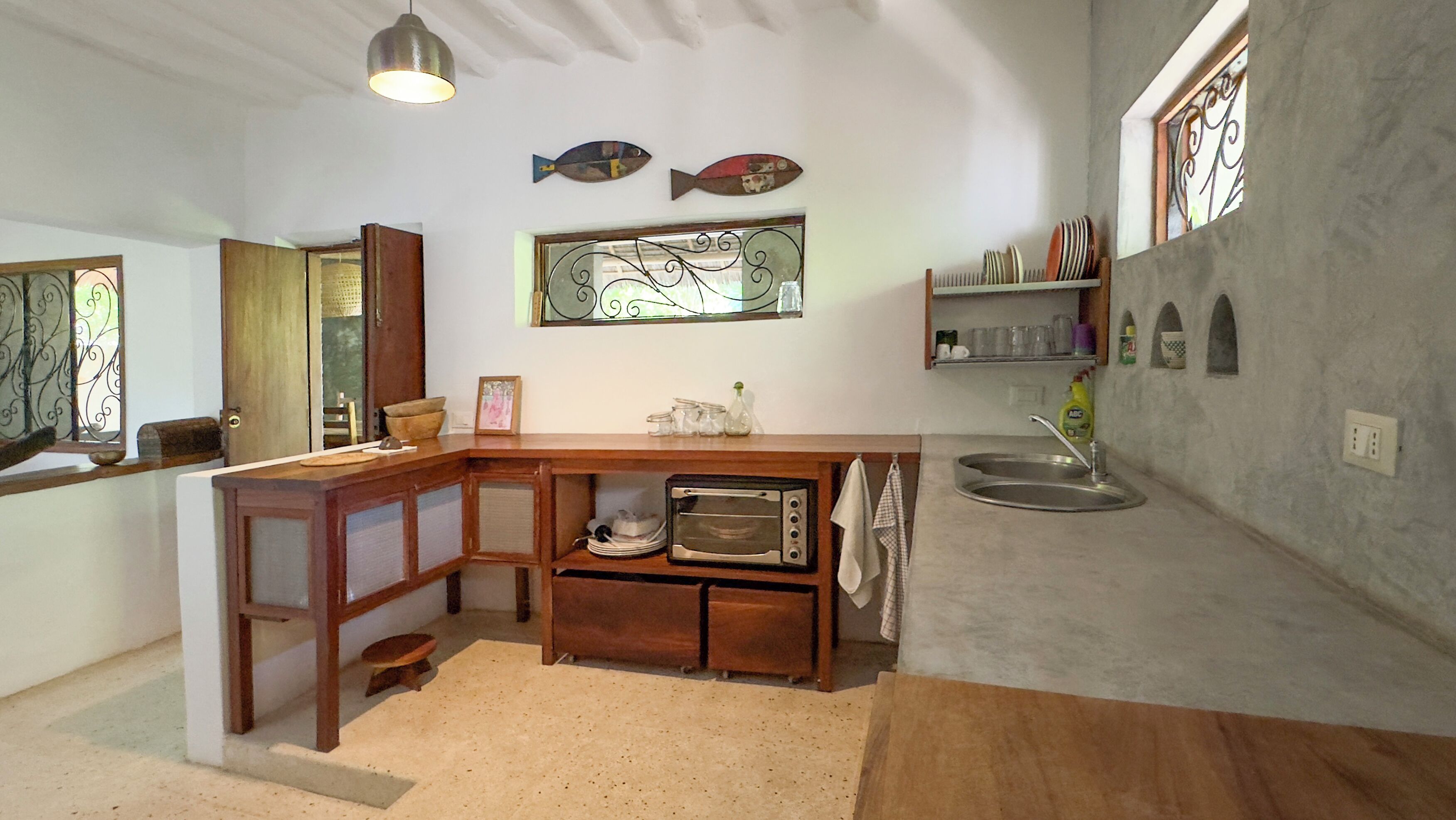 A compact kitchen with a built-in oven, a sink, and a small countertop. There are decorative fish on the wall and a window with a view.