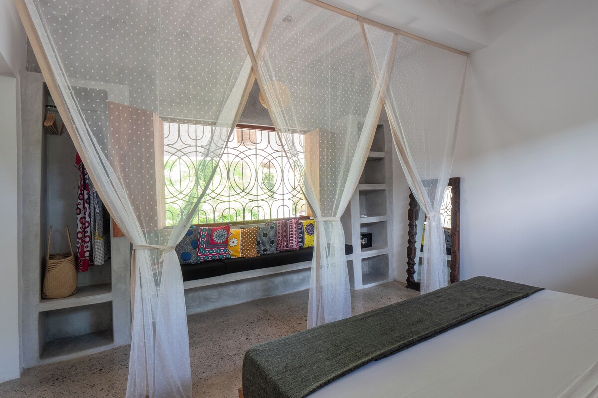 A bedroom with a bed, a bench, a wardrobe, and a window with decorative iron bars.