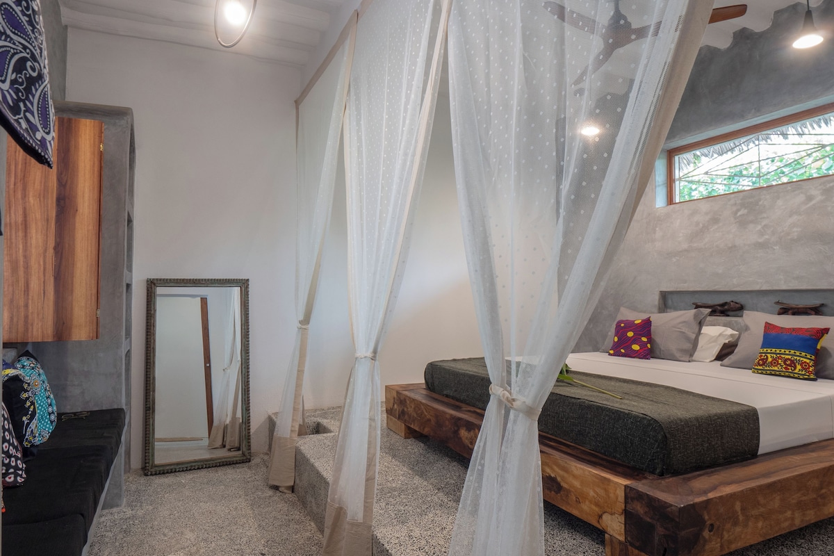 A bedroom with a bed, a window, a mirror, and a curtain.