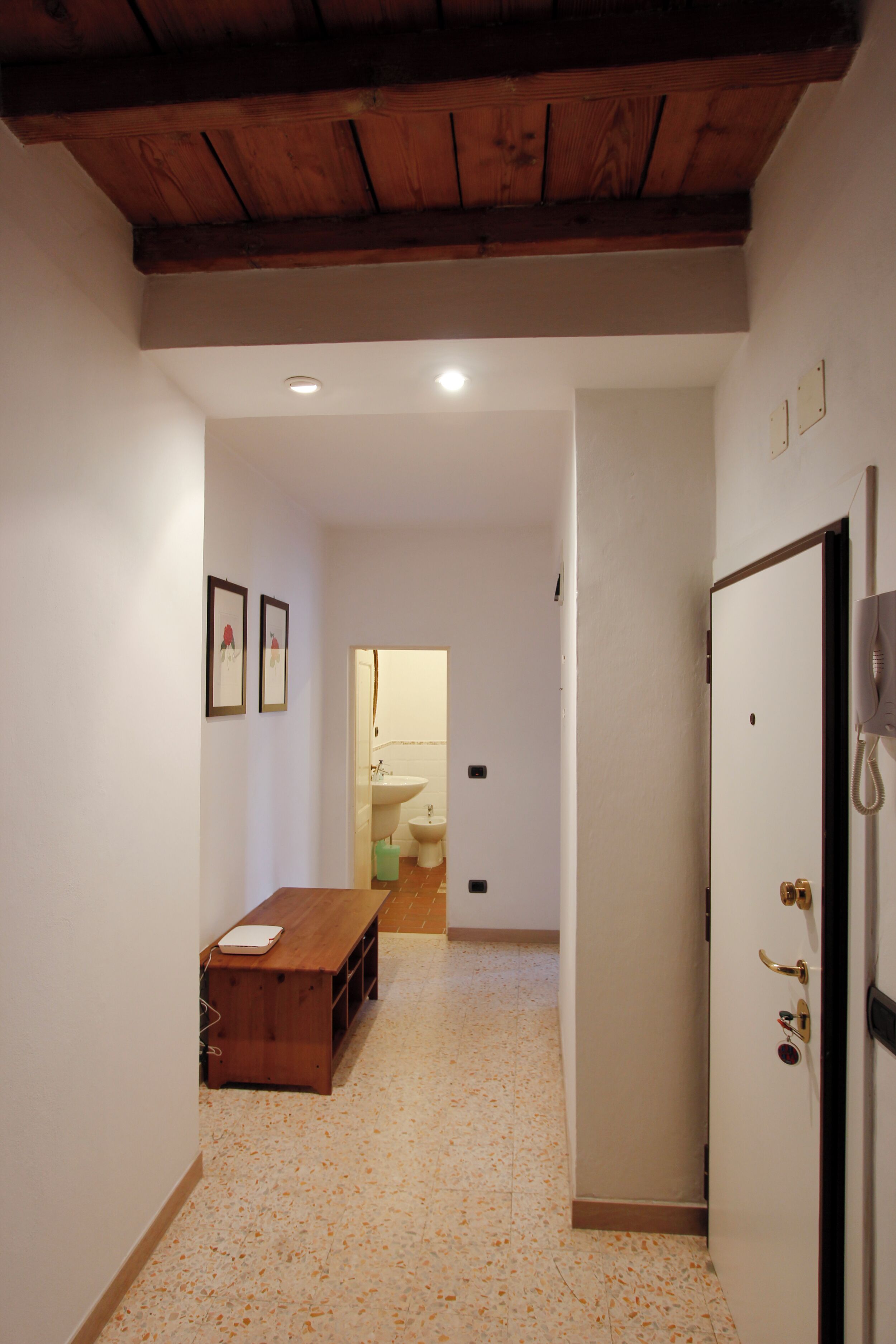 A hallway with a wooden bench, a white door with a phone, and a bathroom visible in the background.